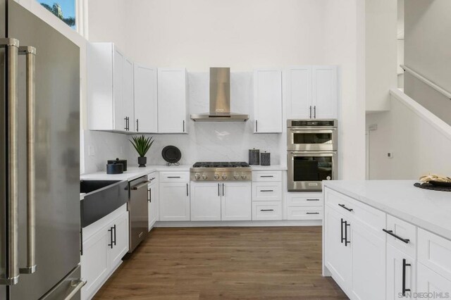 kitchen featuring white cabinetry, wall chimney exhaust hood, stainless steel appliances, and tasteful backsplash