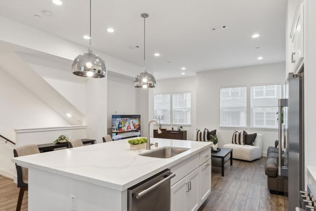 kitchen featuring appliances with stainless steel finishes, decorative light fixtures, sink, white cabinets, and a center island with sink