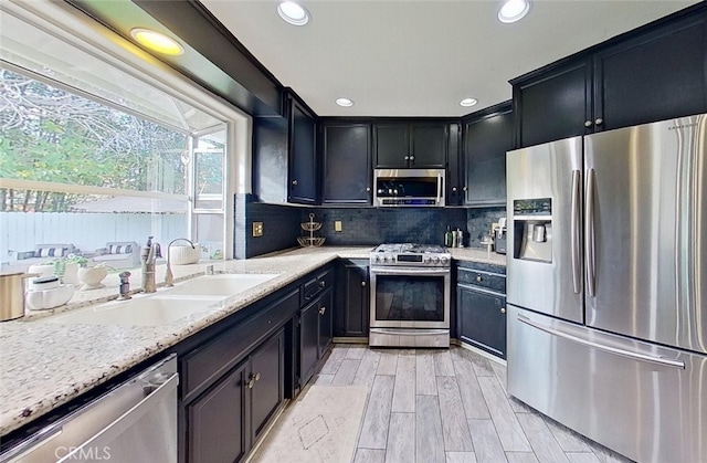 kitchen with stainless steel appliances, backsplash, light stone counters, and sink