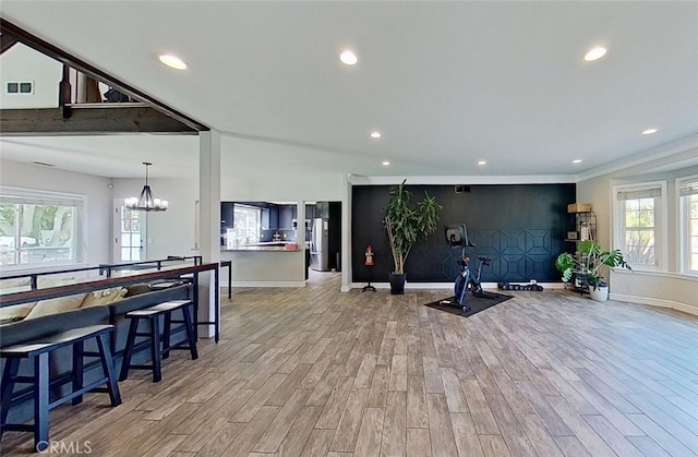 workout area with light wood-type flooring, lofted ceiling, and a notable chandelier