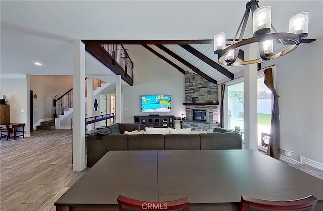 dining area with hardwood / wood-style floors, a stone fireplace, a chandelier, and vaulted ceiling with beams