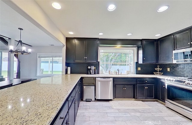 kitchen with stainless steel appliances, plenty of natural light, tasteful backsplash, decorative light fixtures, and light stone countertops