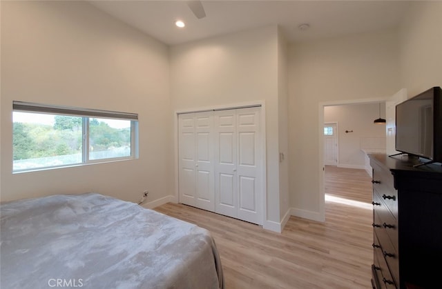 bedroom with ceiling fan, light hardwood / wood-style floors, a closet, and a towering ceiling