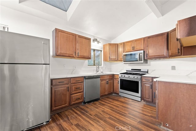 kitchen with a sink, dark wood-style flooring, vaulted ceiling, brown cabinetry, and appliances with stainless steel finishes