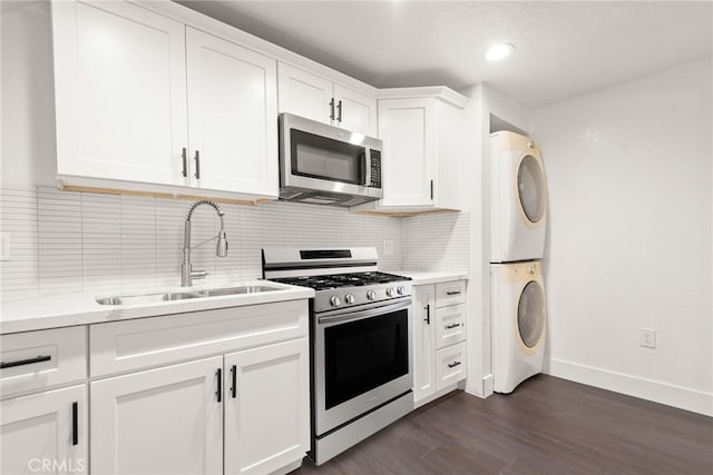 kitchen featuring a sink, stacked washing maching and dryer, dark wood-style flooring, appliances with stainless steel finishes, and white cabinetry