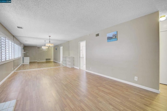 empty room featuring light hardwood / wood-style floors, a textured ceiling, and a chandelier