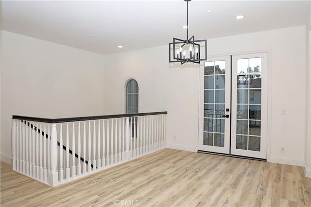 empty room with a notable chandelier, french doors, and light wood-type flooring