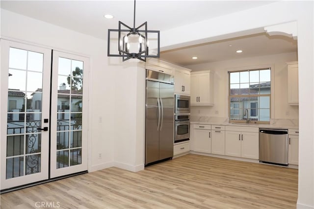 kitchen featuring light wood-type flooring, built in appliances, pendant lighting, sink, and white cabinetry