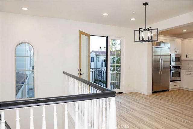 interior space with a chandelier, light wood-type flooring, built in appliances, pendant lighting, and white cabinetry