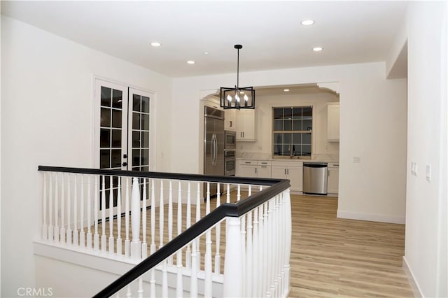 hallway with light wood-type flooring, a notable chandelier, and sink