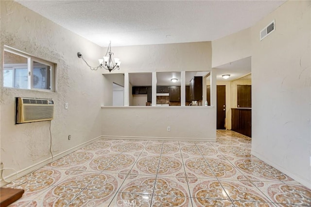 spare room featuring a chandelier, a textured ceiling, light tile patterned floors, and a wall mounted AC