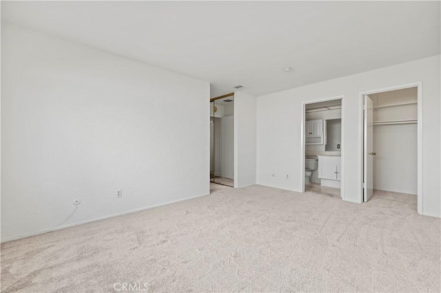 unfurnished bedroom with a spacious closet, light colored carpet, and ensuite bath