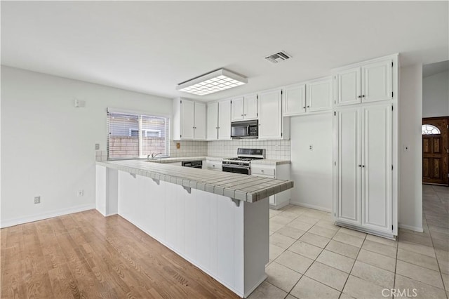 kitchen featuring backsplash, black appliances, kitchen peninsula, tile counters, and white cabinets