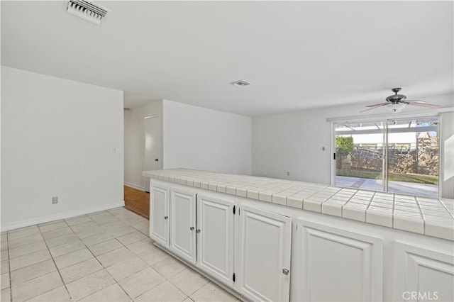 kitchen featuring light tile patterned floors, tile countertops, white cabinets, and ceiling fan