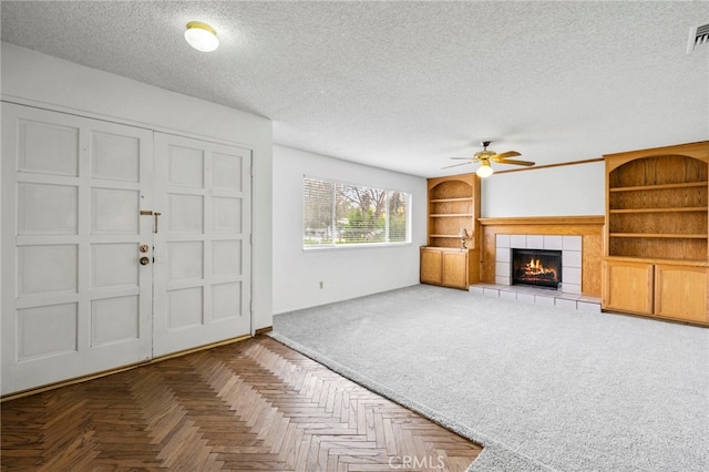 interior space with parquet flooring, ceiling fan, a tiled fireplace, a textured ceiling, and built in shelves