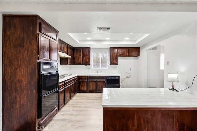 kitchen with dark brown cabinetry, black appliances, light hardwood / wood-style floors, sink, and a tray ceiling