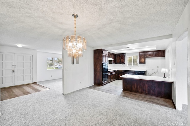 kitchen featuring light colored carpet, kitchen peninsula, dark brown cabinetry, and a notable chandelier