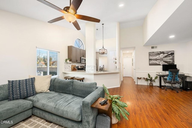 living room featuring ceiling fan with notable chandelier, sink, a towering ceiling, and light wood-type flooring