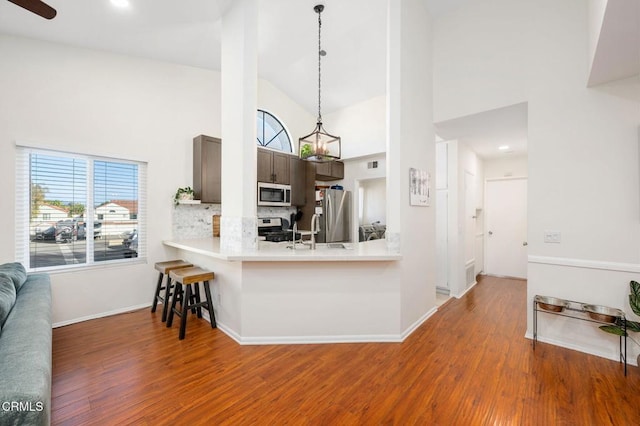 kitchen featuring hardwood / wood-style floors, appliances with stainless steel finishes, kitchen peninsula, high vaulted ceiling, and a breakfast bar