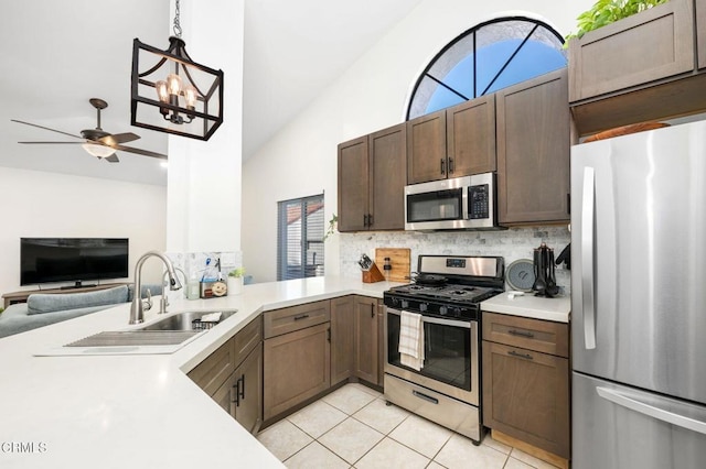 kitchen with appliances with stainless steel finishes, decorative light fixtures, tasteful backsplash, kitchen peninsula, and light tile patterned floors