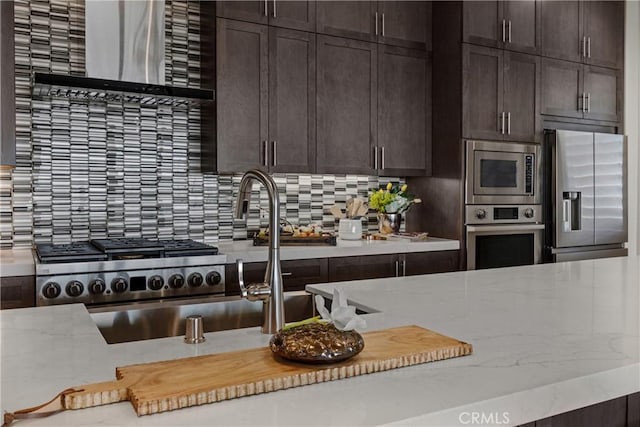 kitchen featuring stainless steel appliances, backsplash, dark brown cabinetry, and light stone countertops