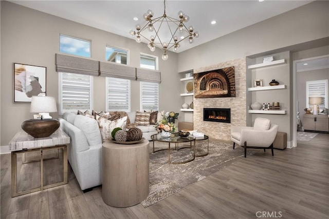 living room with a notable chandelier, wood-type flooring, a stone fireplace, and built in shelves