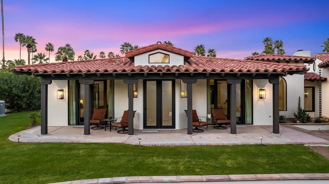 back house at dusk with a lawn and a patio