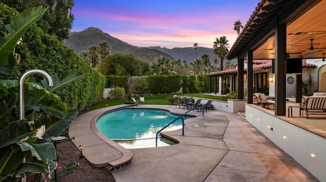 pool at dusk featuring a mountain view, a patio area, and ceiling fan