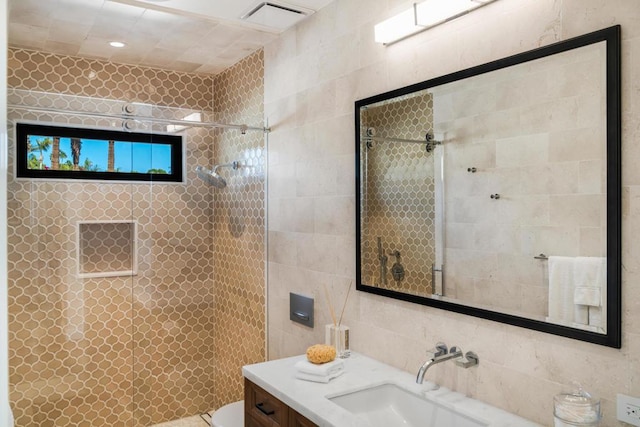 bathroom with toilet, vanity, tile walls, and a tile shower