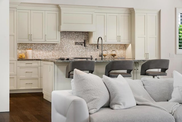 kitchen featuring tasteful backsplash, dark wood-type flooring, stone counters, cream cabinets, and sink