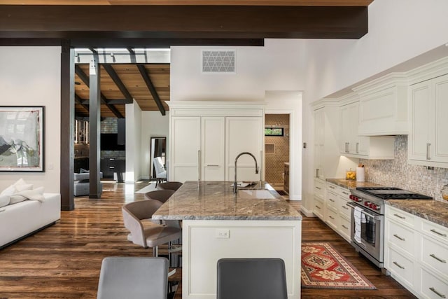 kitchen with designer range, sink, dark stone counters, and a kitchen island with sink