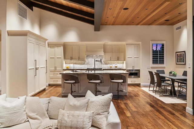 kitchen with dark stone counters, a kitchen breakfast bar, wooden ceiling, a center island with sink, and beam ceiling