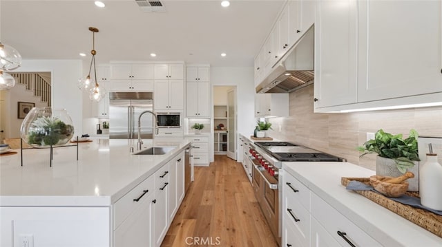 kitchen featuring white cabinetry, decorative light fixtures, a kitchen island with sink, high quality appliances, and sink