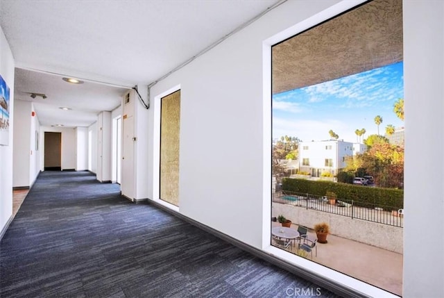 hallway featuring plenty of natural light and dark colored carpet