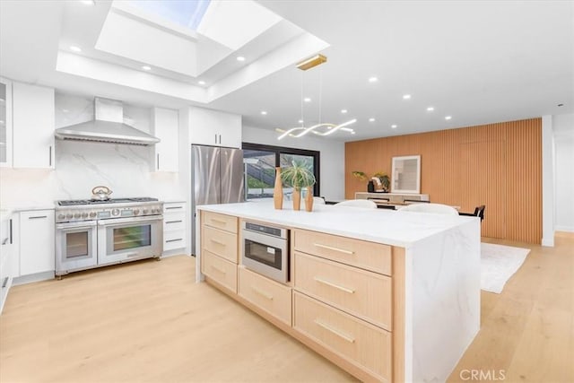 kitchen featuring white cabinetry, stainless steel appliances, wall chimney range hood, a kitchen island, and pendant lighting