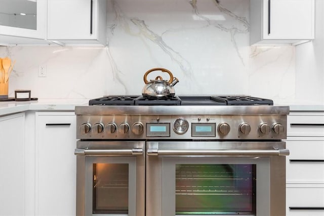 kitchen featuring high end stove, backsplash, and white cabinetry