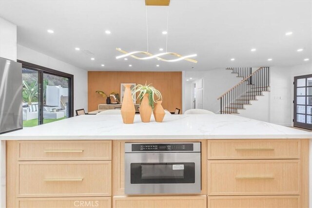 kitchen with pendant lighting, a center island, stainless steel oven, a kitchen breakfast bar, and light brown cabinets