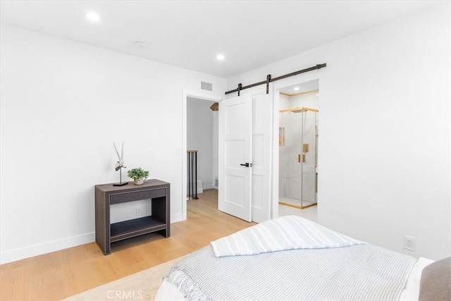 bedroom featuring a barn door, connected bathroom, and light hardwood / wood-style floors