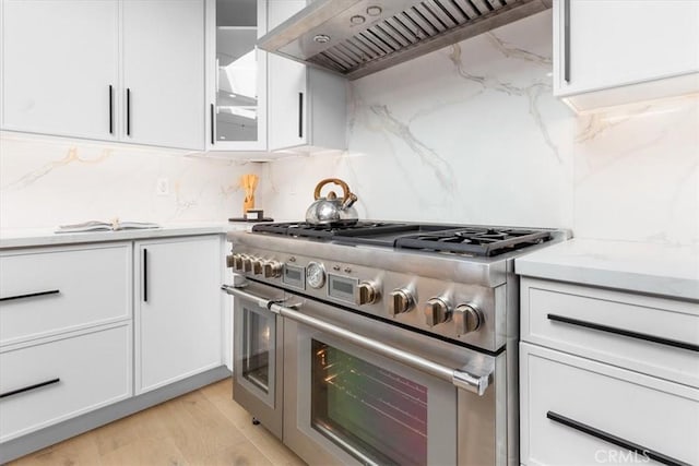 kitchen featuring double oven range, premium range hood, decorative backsplash, light wood-type flooring, and white cabinets