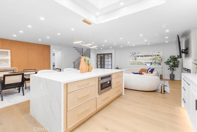 kitchen with wall oven, decorative light fixtures, light brown cabinetry, a kitchen island, and light hardwood / wood-style flooring