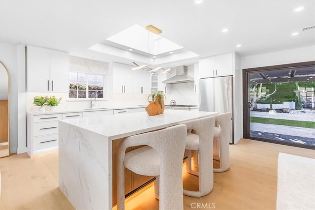 kitchen featuring wall chimney range hood, white cabinets, and a center island