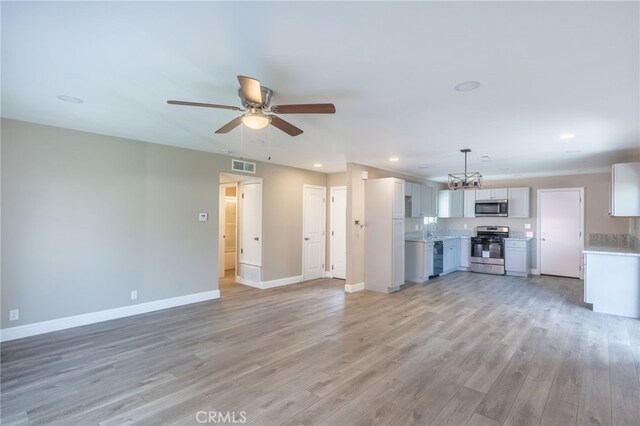 unfurnished living room with ceiling fan with notable chandelier and light hardwood / wood-style flooring