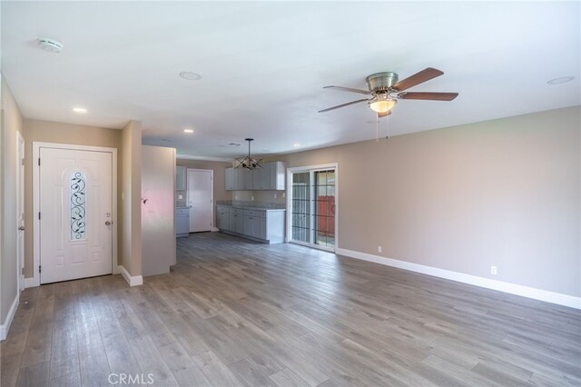 unfurnished living room featuring ceiling fan with notable chandelier and light hardwood / wood-style flooring