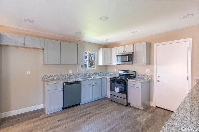 kitchen featuring light wood-type flooring, appliances with stainless steel finishes, sink, and light stone counters