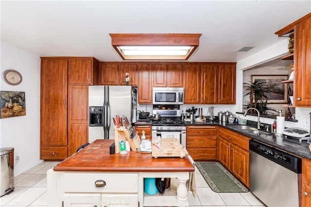 kitchen with light tile patterned flooring, appliances with stainless steel finishes, dark stone counters, and sink