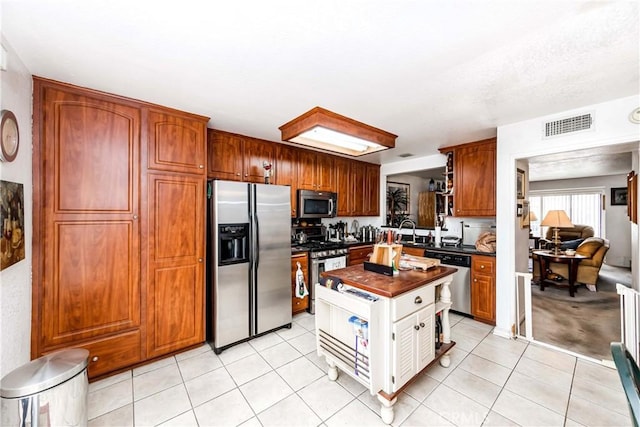 kitchen with wooden counters, light tile patterned floors, appliances with stainless steel finishes, and sink