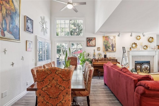 dining space featuring a towering ceiling, a fireplace, rail lighting, hardwood / wood-style flooring, and ceiling fan