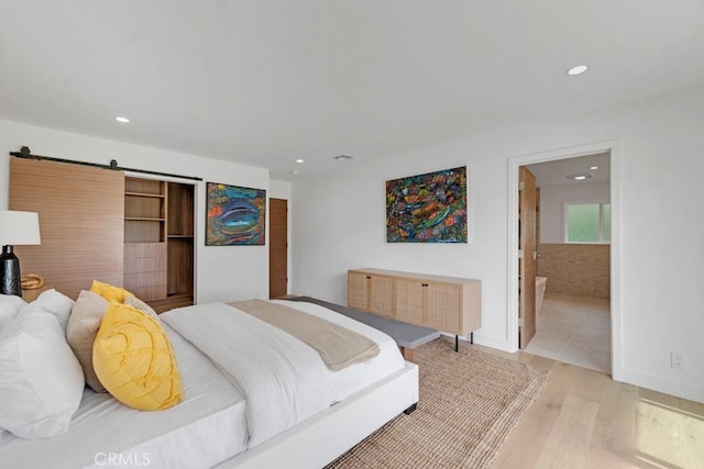 bedroom with light wood-type flooring, a barn door, and ensuite bath