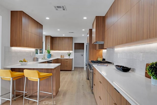 kitchen with a breakfast bar, backsplash, high end range, and light wood-type flooring