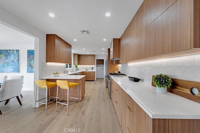 kitchen featuring high end stainless steel range oven, light hardwood / wood-style flooring, backsplash, and a breakfast bar